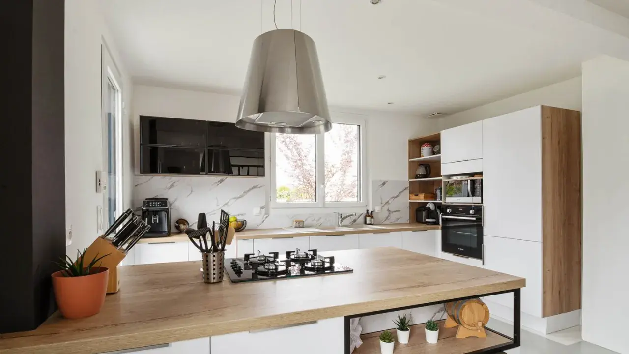 Cuisine moderne avec îlot central en bois, hotte design en alliage inox, et électroménagers intégrés.