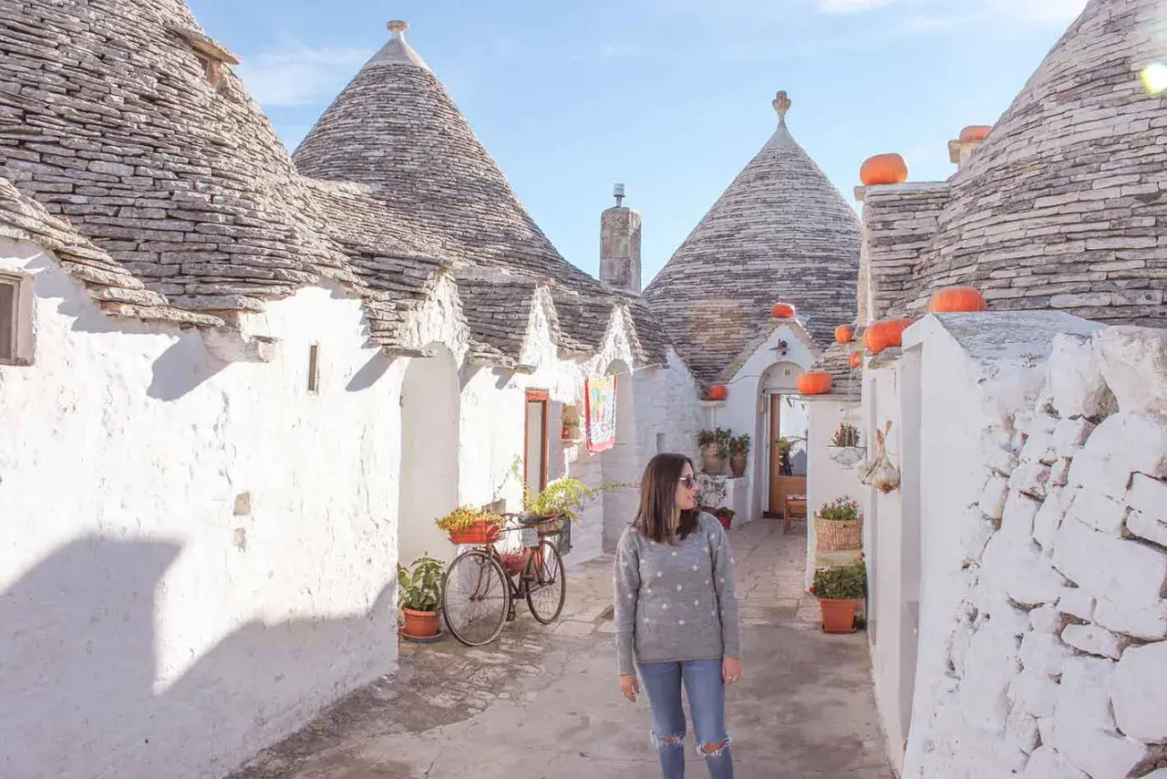 Una donna passeggia tra i trulli di Alberobello, un'icona di cosa vedere in Puglia. Le case coniche e i colori vivaci creano un'atmosfera magica.