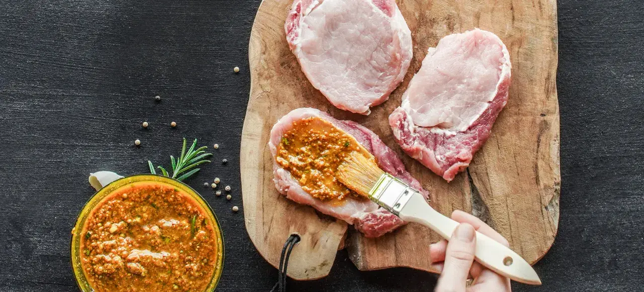 Frisches **Schweinefleisch marinieren** für zarte Steaks. Eine würzige Marinade wird mit einem Pinsel aufgetragen.