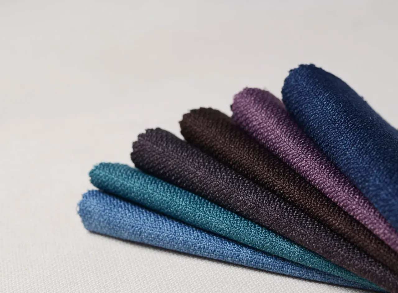 Échantillons de tissus aux teintes profondes, évoquant la richesse des 15 fibres naturelles. Bleu, turquoise, violet, marron.