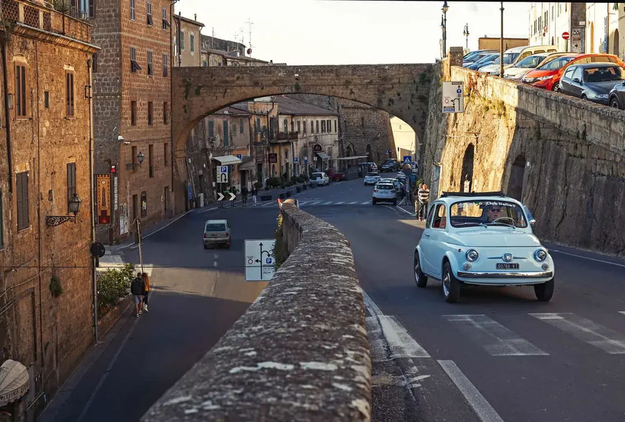 A light blue Fiat 500 drives through a Tuscan town. Do you need a car in Florence to explore charming streets like this?