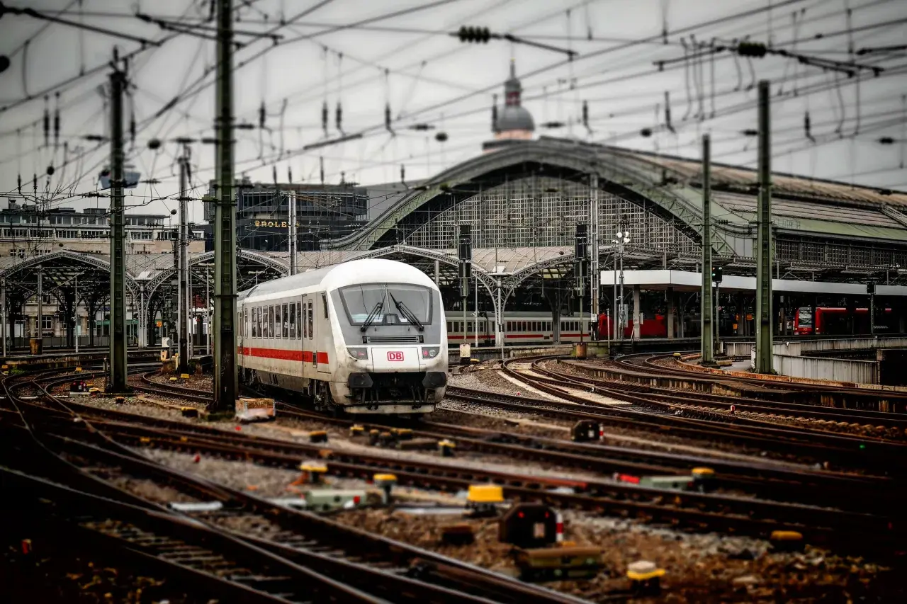Pociąg DB na stacji, skomplikowana sieć torów i trakcji elektrycznej. Widoczna blokada liniowa sygnalizuje gotowość do odjazdu.