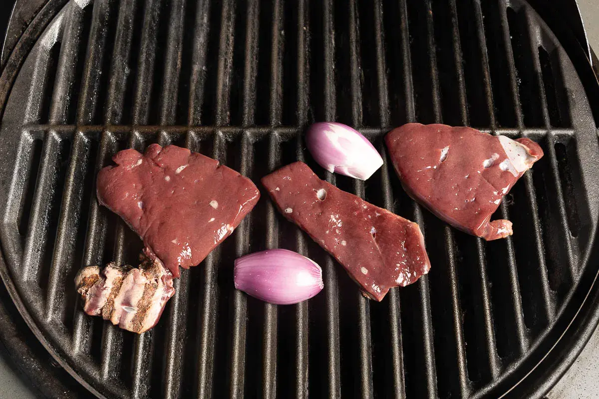 Rohe Leberstücke und Schalotten liegen bereit zum leber grillen auf einem heißen Rost.