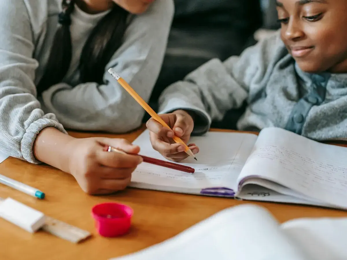 Dos niños concentrados en su dictado de 3 primaria, escribiendo en un cuaderno con lápices.