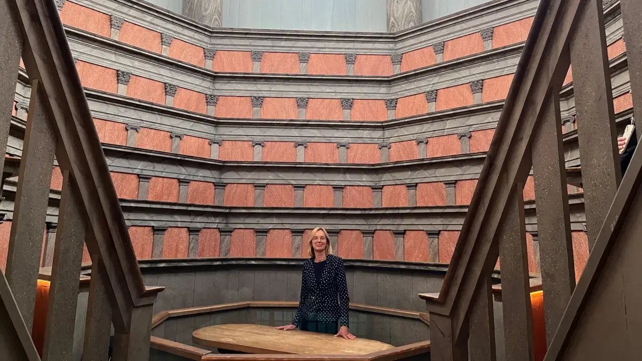 En kvinna står i den imponerande **anatomiska teatern Uppsala**. De rödbruna väggarna med sina pelare skapar en unik atmosfär.