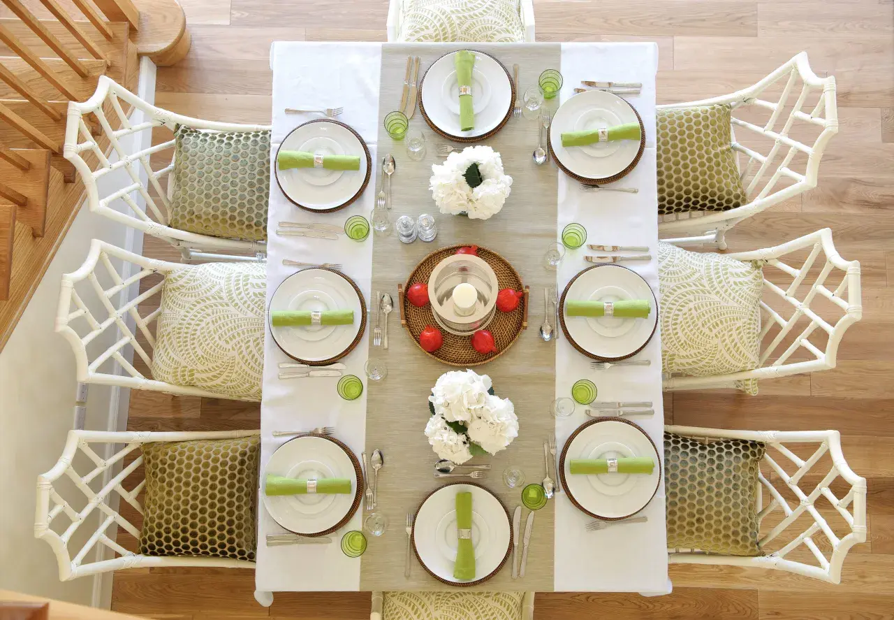 Tavola apparecchiata per una festa a tema chic, con sedie in bambù bianco e cuscini decorati.