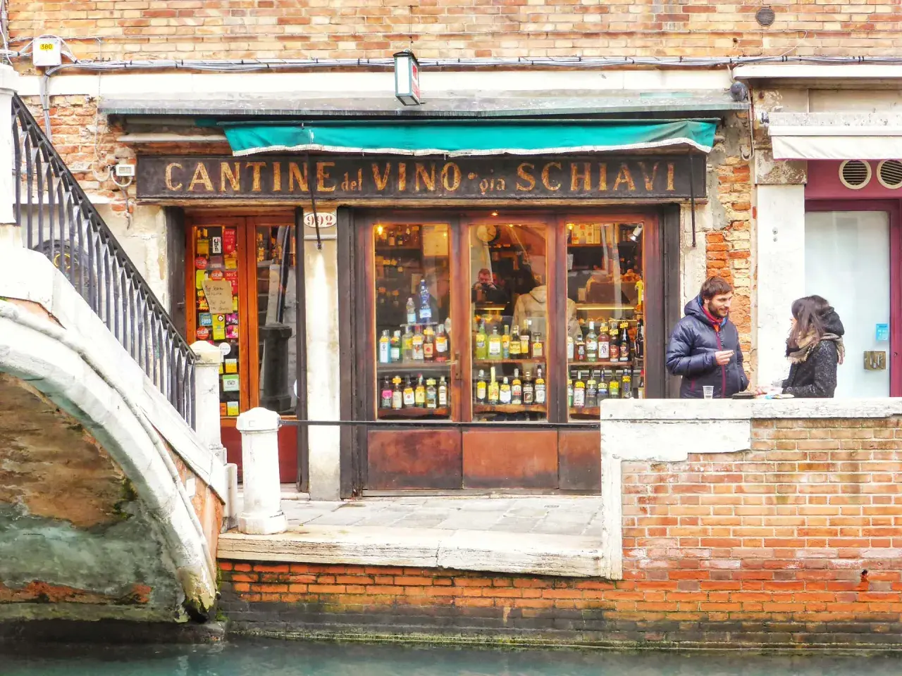 Cantina del Vino, un posto ideale per mangiare a Venezia spendendo poco. Coppia parla davanti al locale pieno di bottiglie.