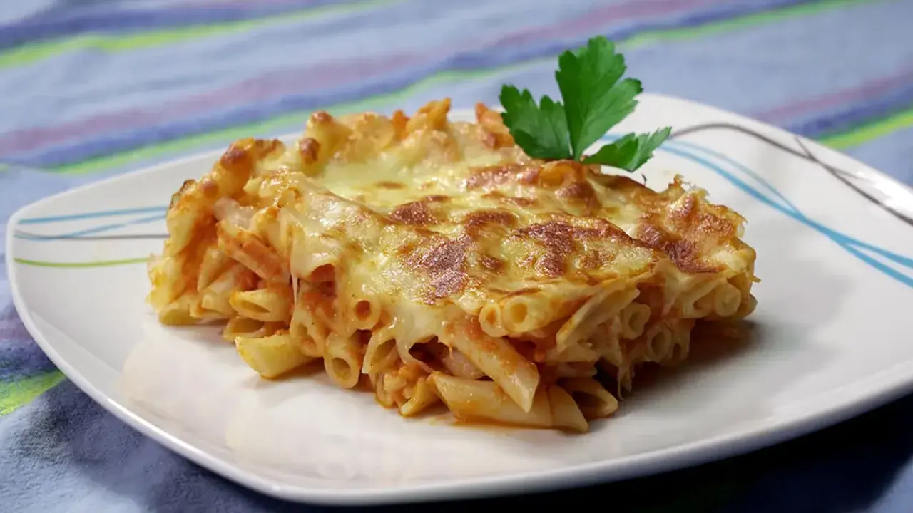 Porción de macarrones al horno gratinados con queso derretido y una hoja de perejil, servida en un plato blanco.