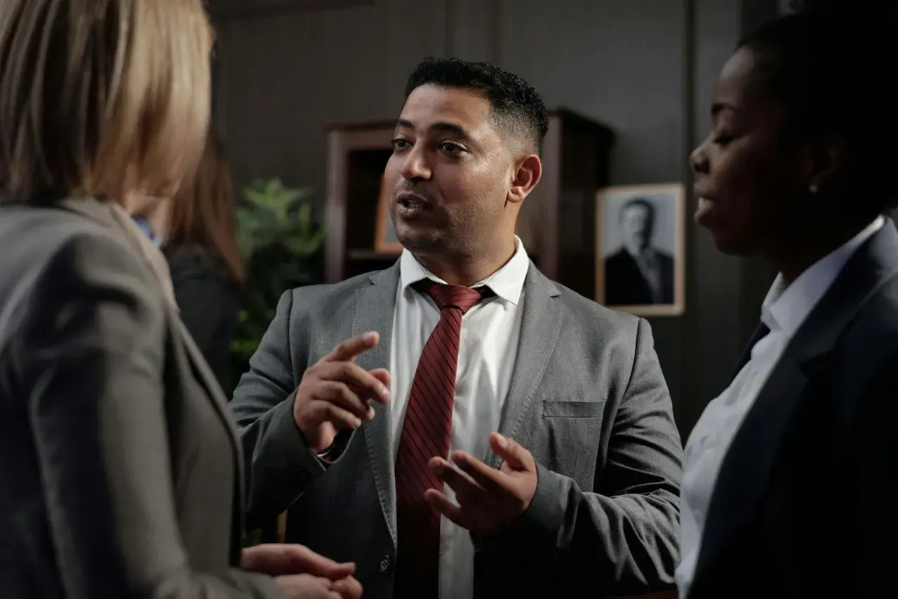 Un homme en costume explique avec passion à deux femmes, peut-être une affaire où ils risquent d'être déboutés en justice.