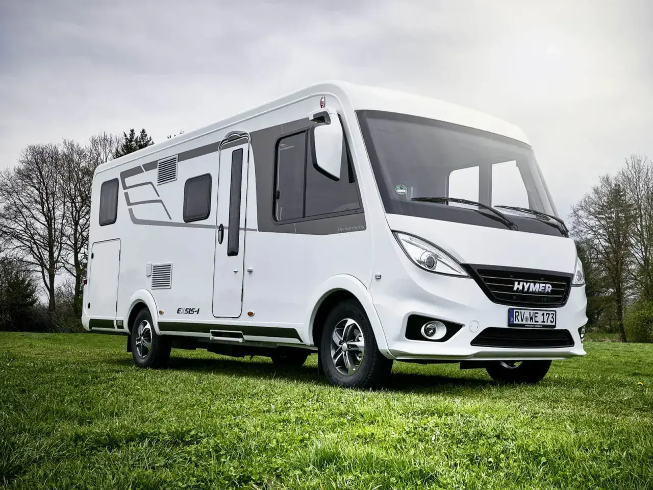 Biała kamper z serii Hymermobil, produkt Erwin Hymer Group, stoi na zielonej trawie.