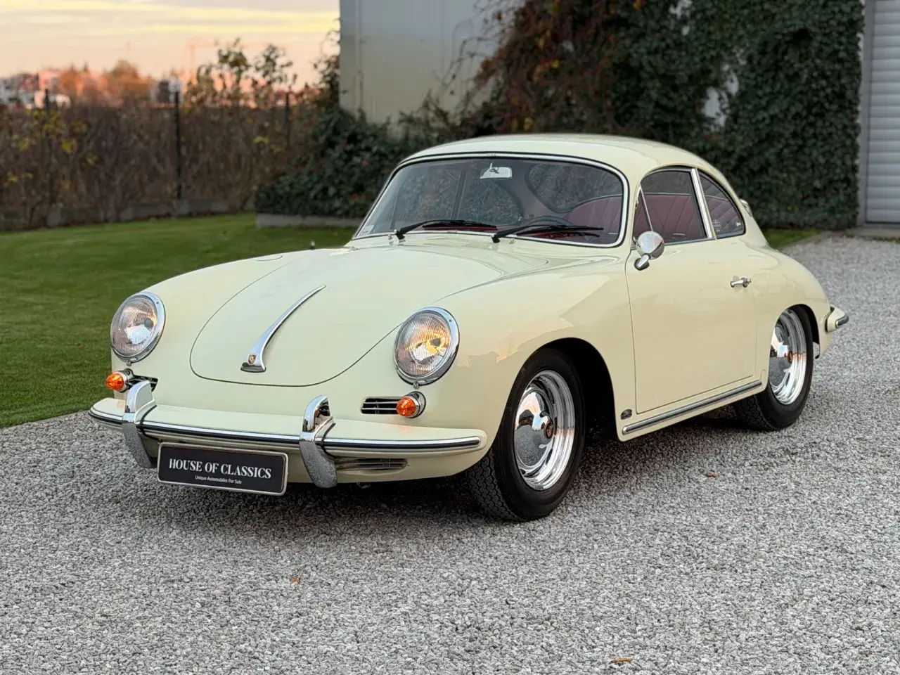 Klasyczny kremowy Porsche 356 z czerwoną tapicerką, zaparkowany na żwirowej nawierzchni.