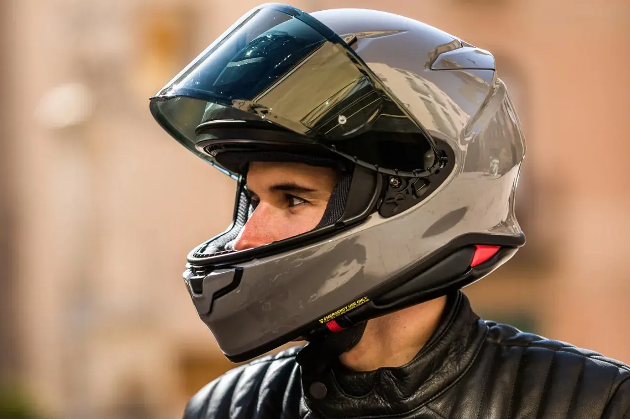 Hombre con casco moto 125 gris brillante, visor oscuro y chaqueta de cuero negra.