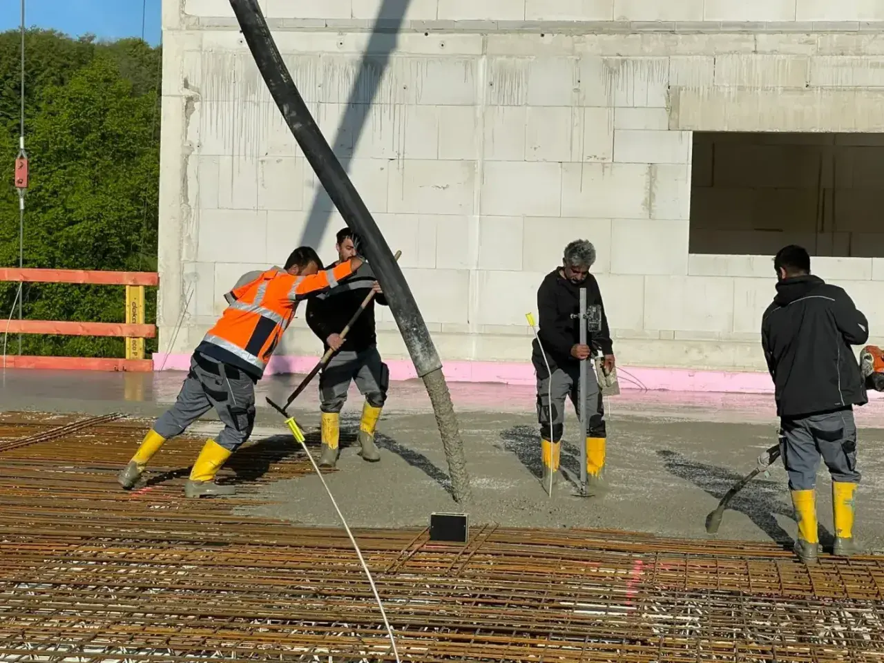 Arbeiter gießen Beton für die Bodenplatte. Sie schalen die Platte aus und verteilen den frischen Beton mit Werkzeugen.