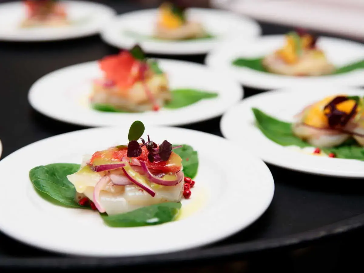 Carpaccio de saint jacques frais, garni de pamplemousse, oignons rouges et pousses sur des feuilles d'épinards.