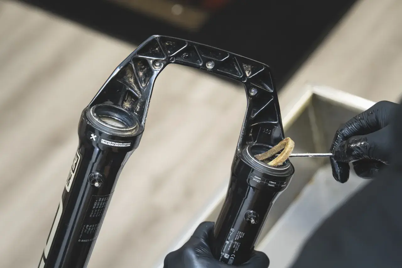 Gloved hands clean a RockShox Revelation RC fork, removing dirt from the stanchions.
