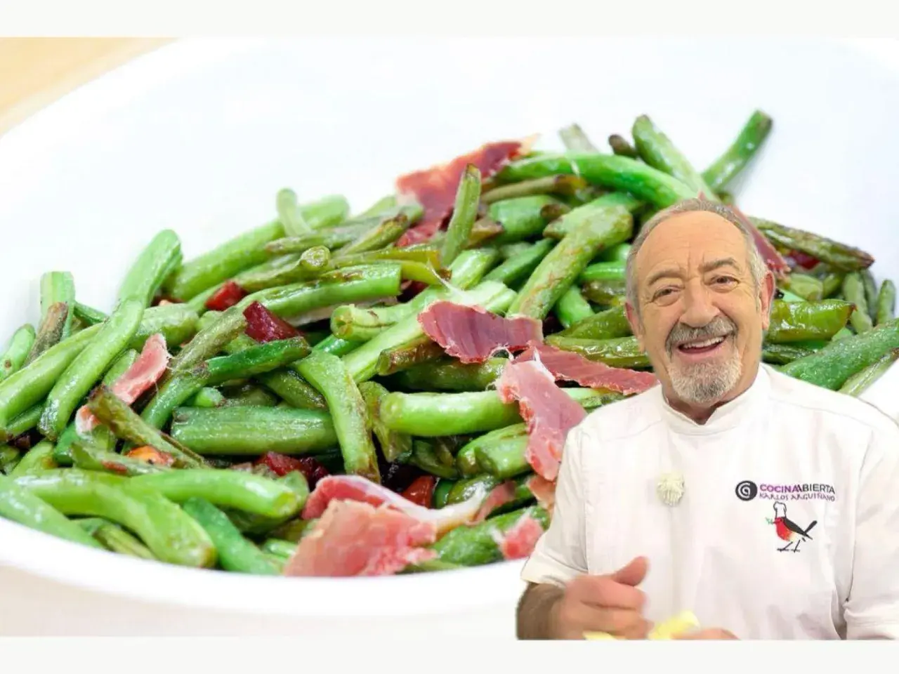 Un chef sonriente presenta un plato de judías verdes salteadas con trozos de jamón.