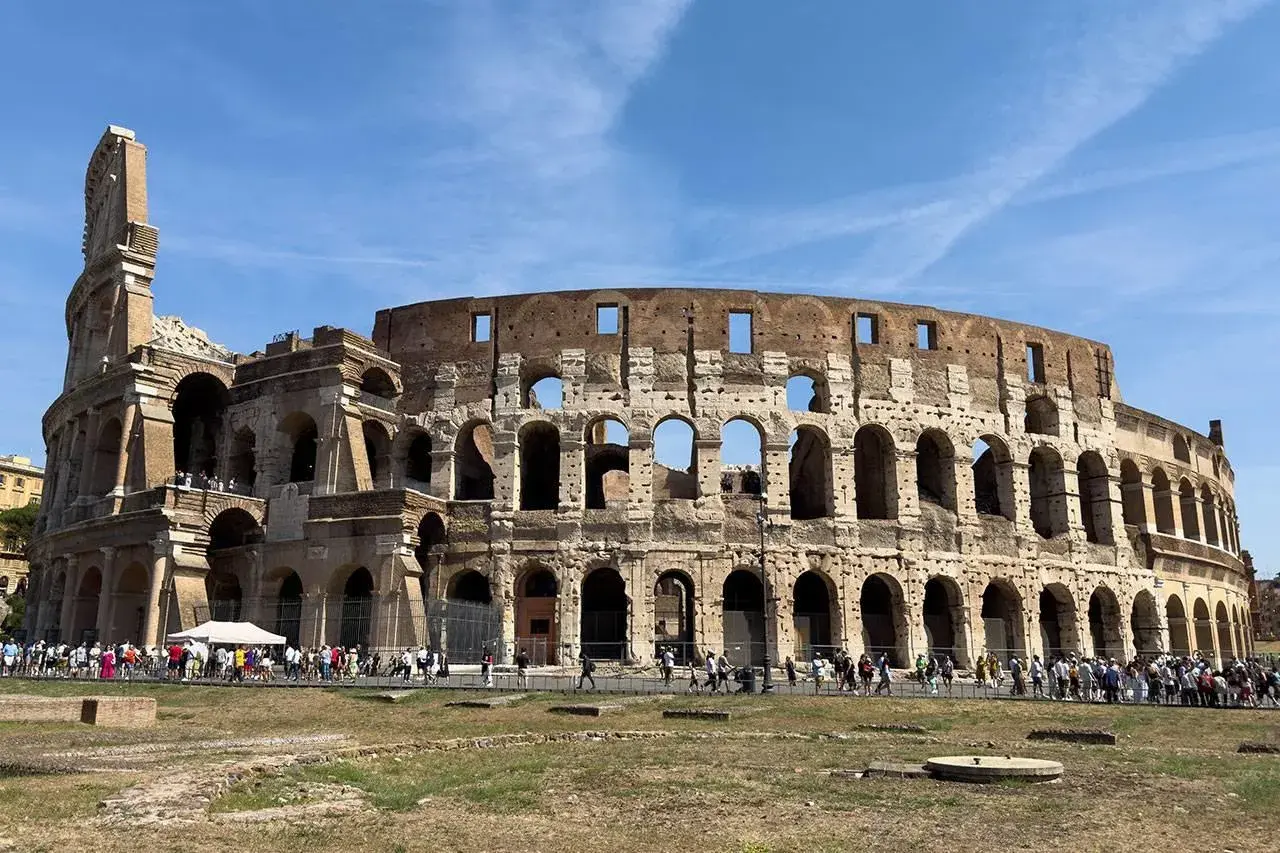 Il Colosseo, una delle principali attrazioni di Roma, 10 cose da vedere. Turisti ammirano l'anfiteatro romano sotto un cielo azzurro.