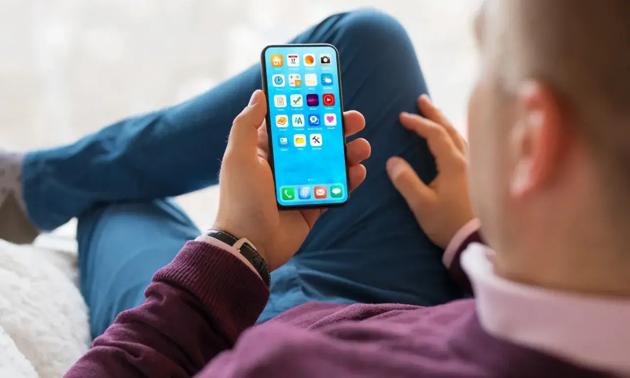 Dłoń trzyma smartfon z ikonami aplikacji. Szybkość ładowania telefonu zależy od wielu czynników, np. ładowarki i stanu baterii.