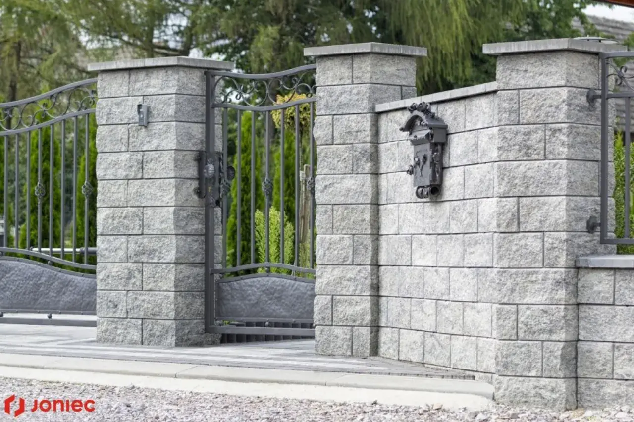 Betonowy słupek z zamontowaną skrzynką na listy i fragmentem metalowej furtki.