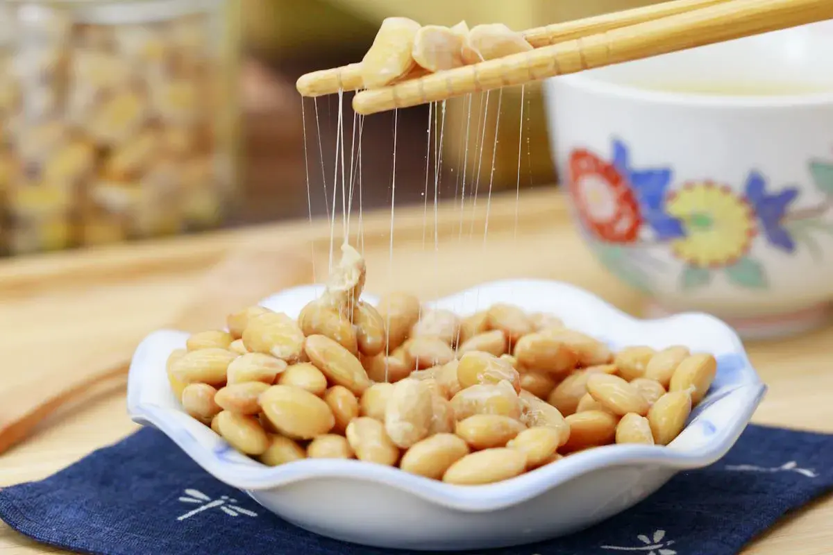 Fermentierte Sojabohnen, auch Natto genannt, werden mit Stäbchen aus einer Schale gehoben. Die klebrigen Fäden sind charakteristisch.