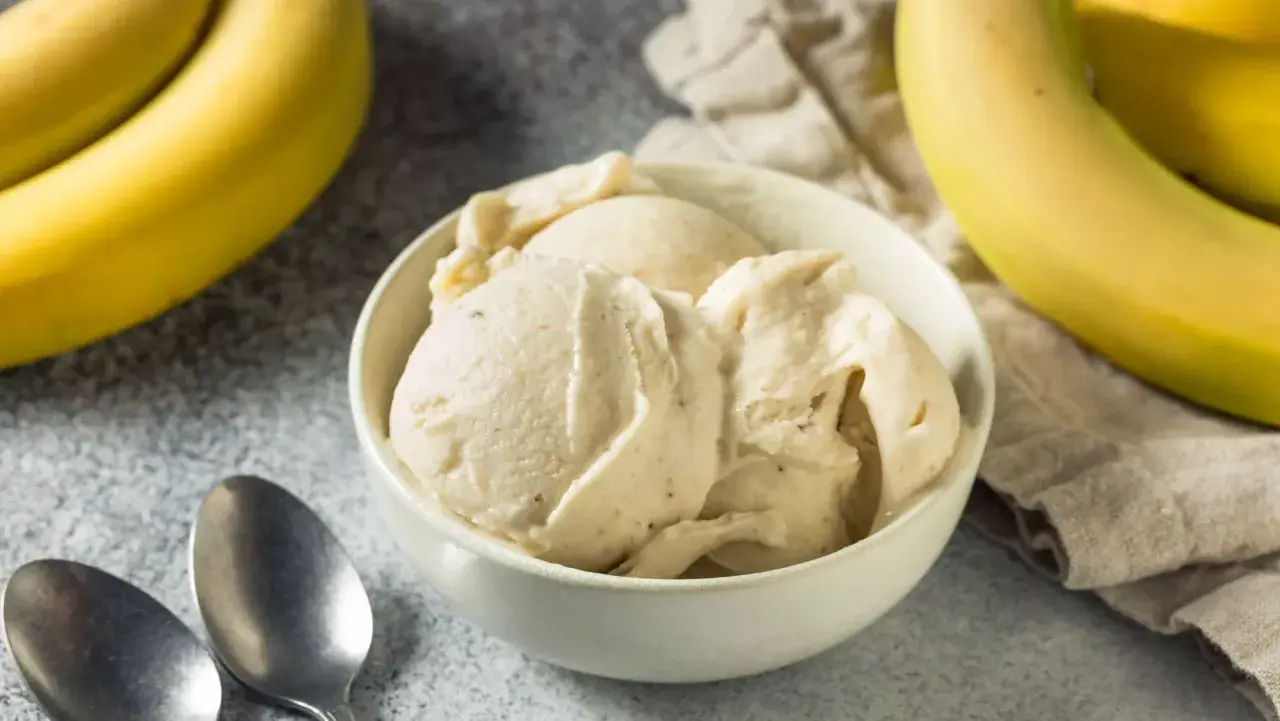 Un cremoso helado de plátano en un tazón blanco, con plátanos amarillos frescos al lado.