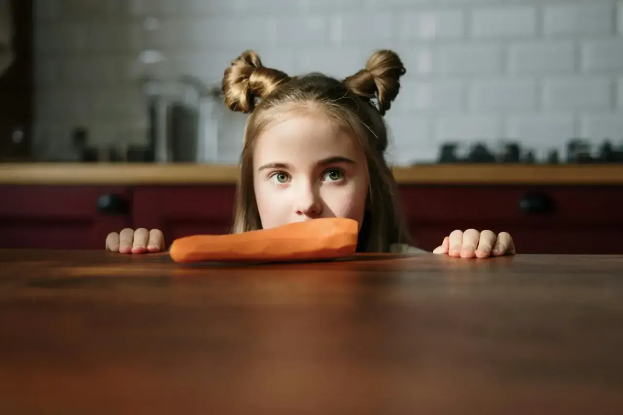 Bambina con acconciatura a ciambella guarda una carota, forse un caso di neofobia alimentare.