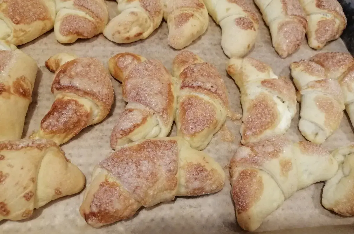 Rogaliki z masą serową, posypane cukrem, pieczone na papierze.