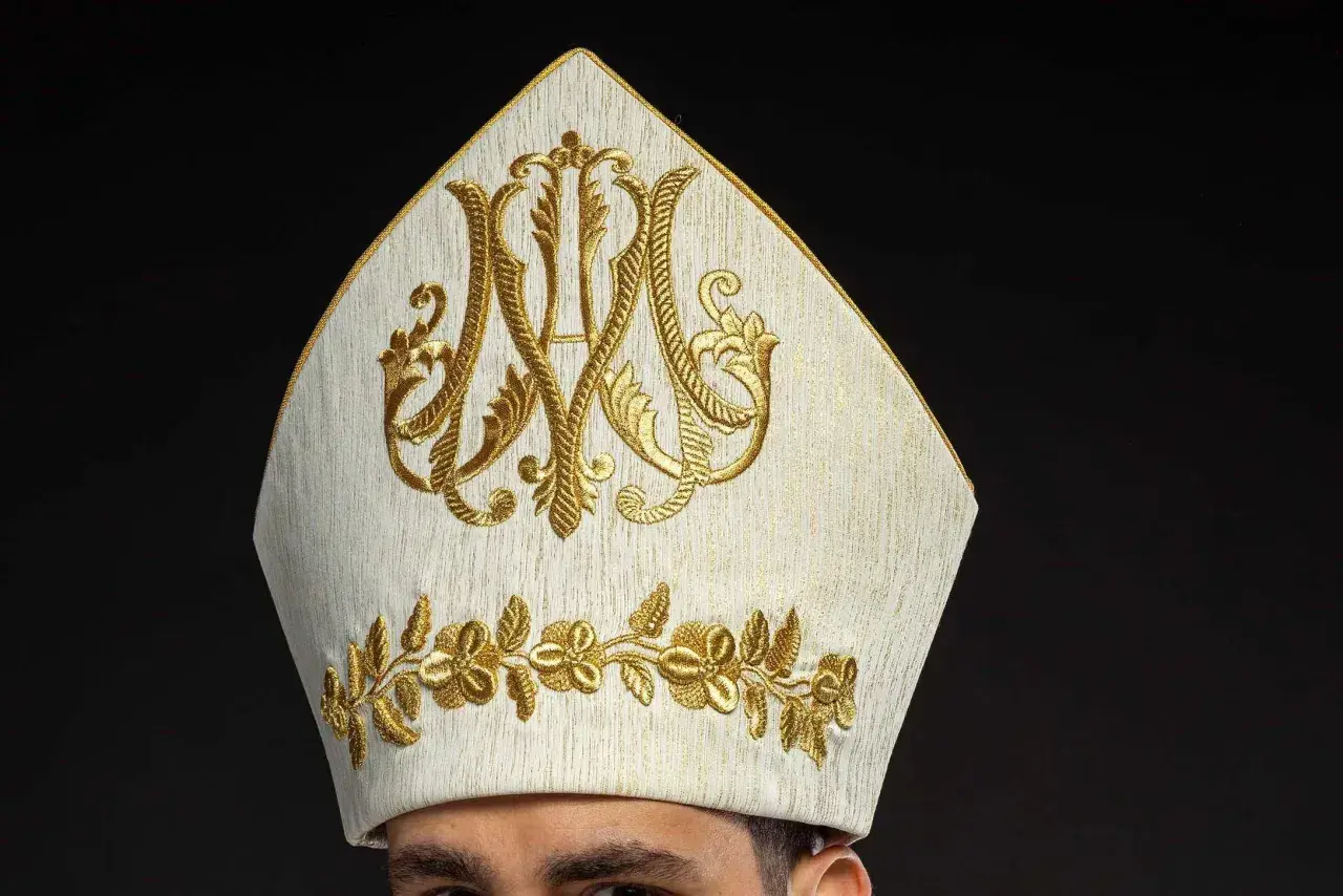 Biała mitra z haftem w kolorze złota, symbolizująca godność. Warto wiedzieć, jak się zwracać do biskupa, by okazać mu szacunek.