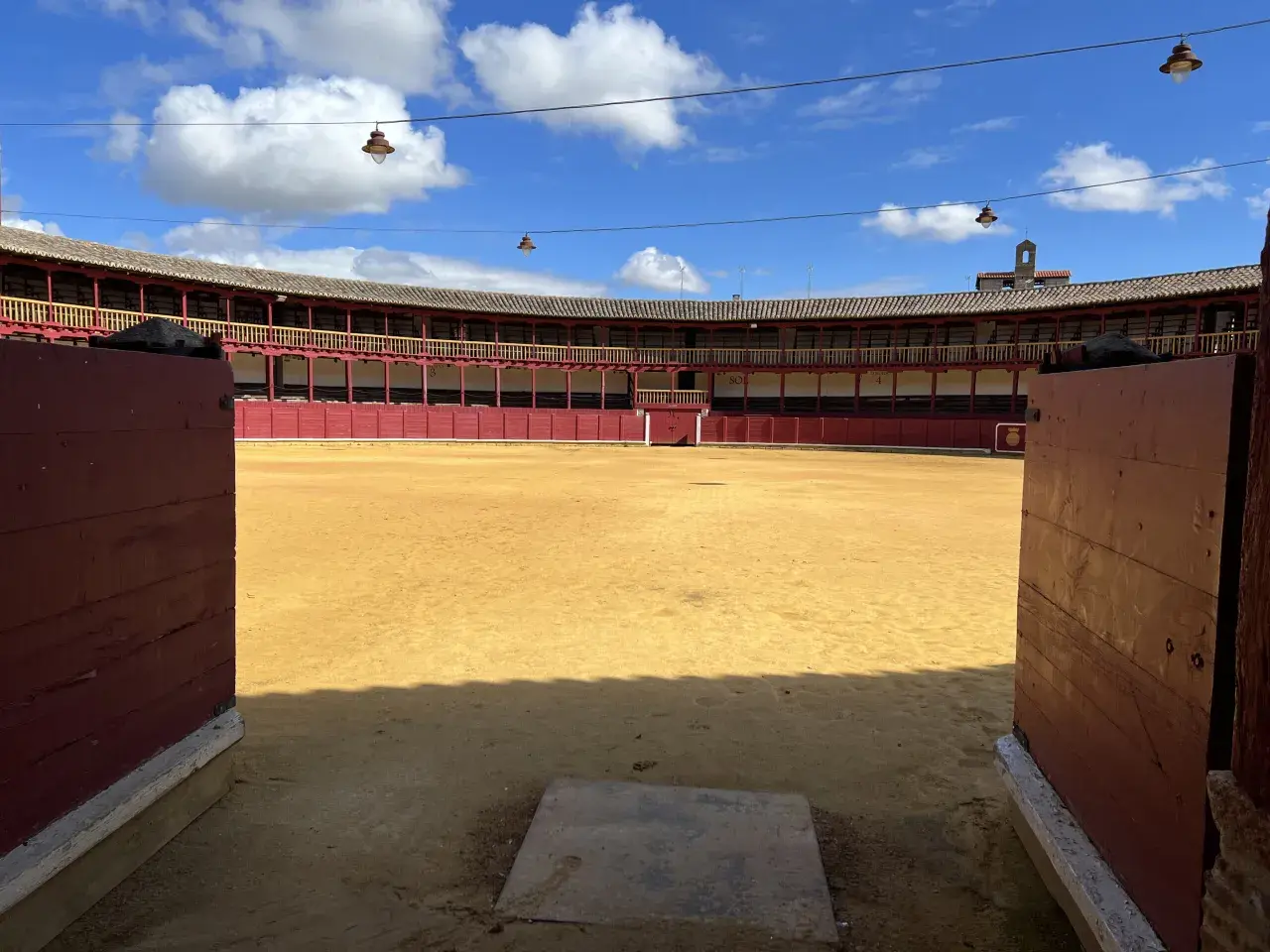 La plaza de toros de Toro, con su arena dorada y gradas rojas, espera bajo un cielo azul con nubes.