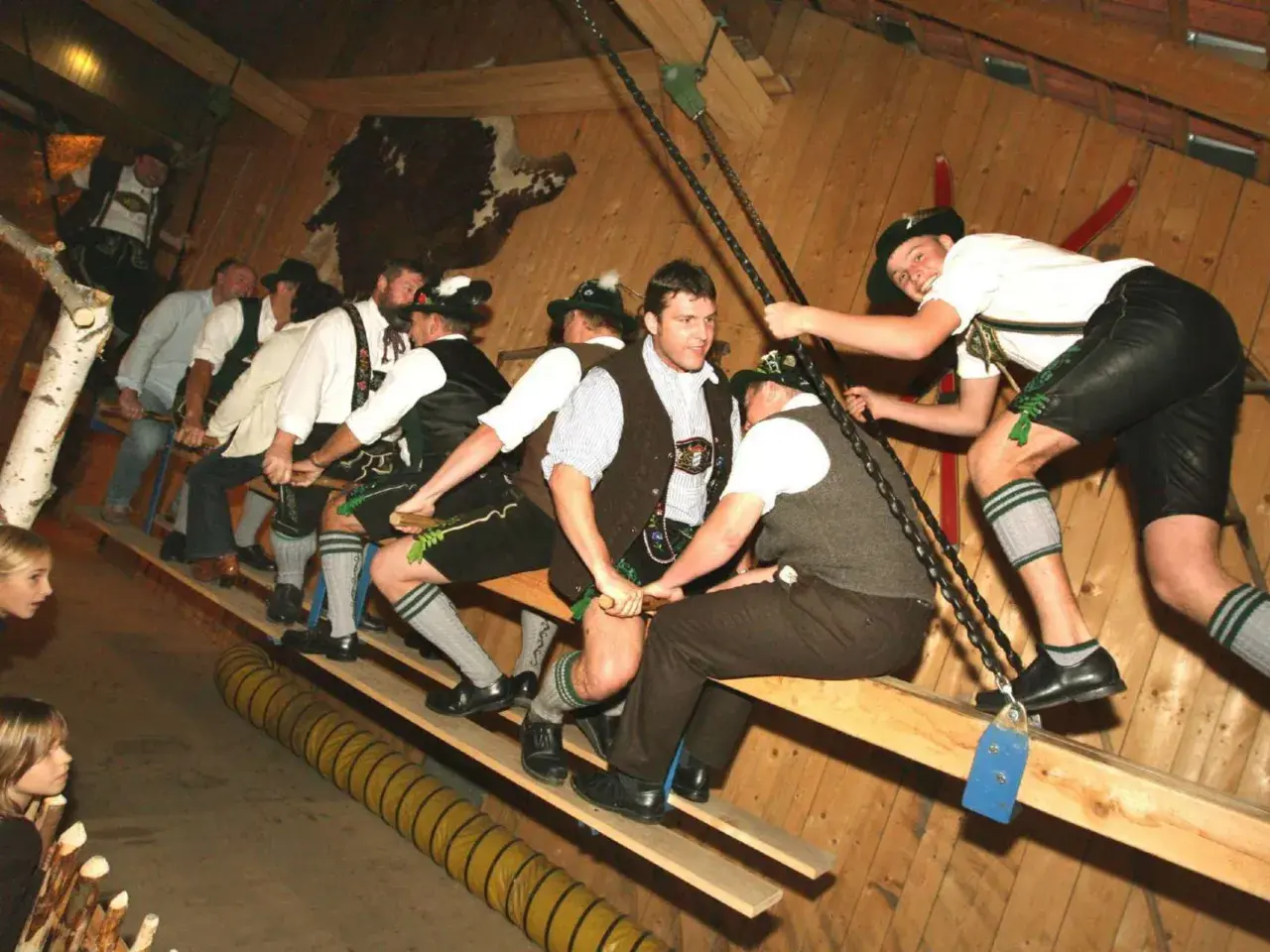 Männer in Lederhosen und Trachtenhemden auf einer Holzbank, bereit für ein Spiel auf der bayrischen Kirchweih.