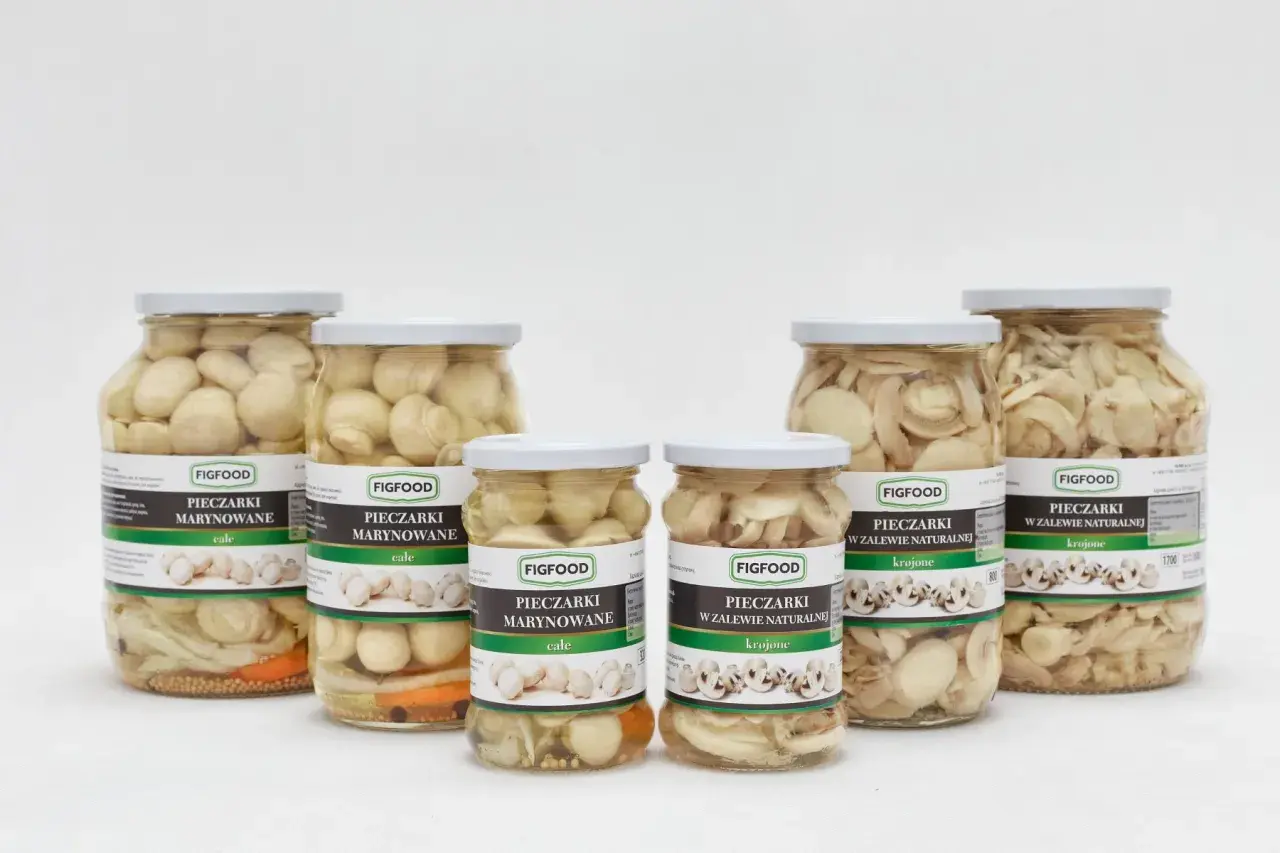 Sześć słoików z marynowanymi pieczarkami Figfood, w tym całe i krojone, na białym tle.