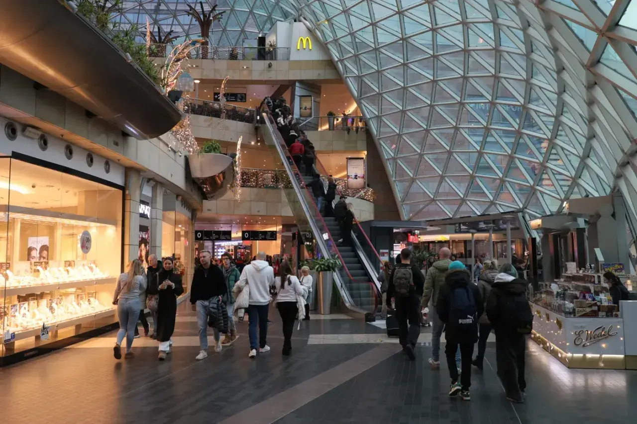 Ludzie w centrum handlowym, schodzą i wchodzą na ruchome schody. Czy 6 stycznia są otwarte sklepy? Widać sklepy z biżuterią i jedzeniem.
