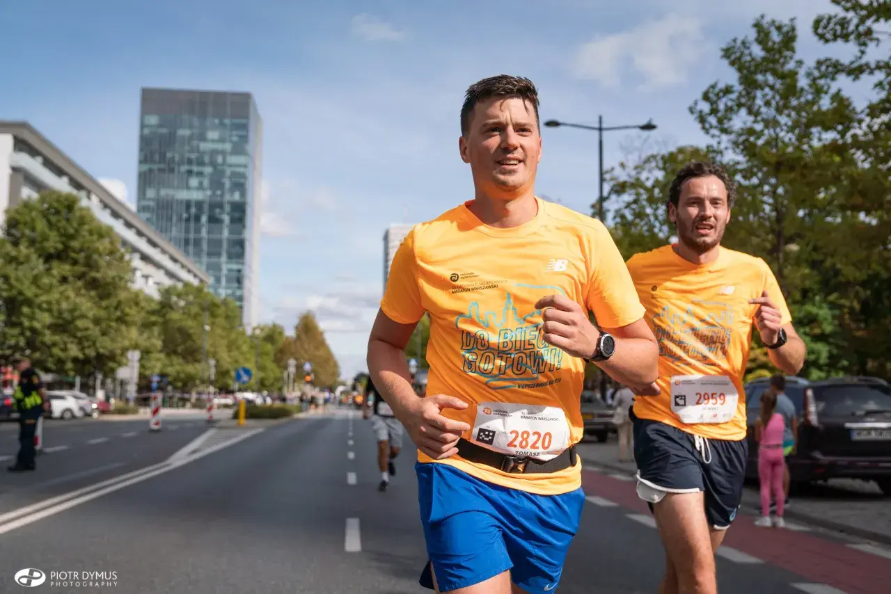 Dwóch biegaczy w pomarańczowych koszulkach na ulicach Warszawy podczas maratonu. Czy to już 42 maraton ile km?