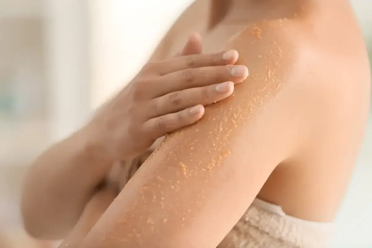 Mano che applica scrub corpo per esfoliare e rendere la pelle liscia e luminosa. Scopri a cosa serve lo scrub corpo.