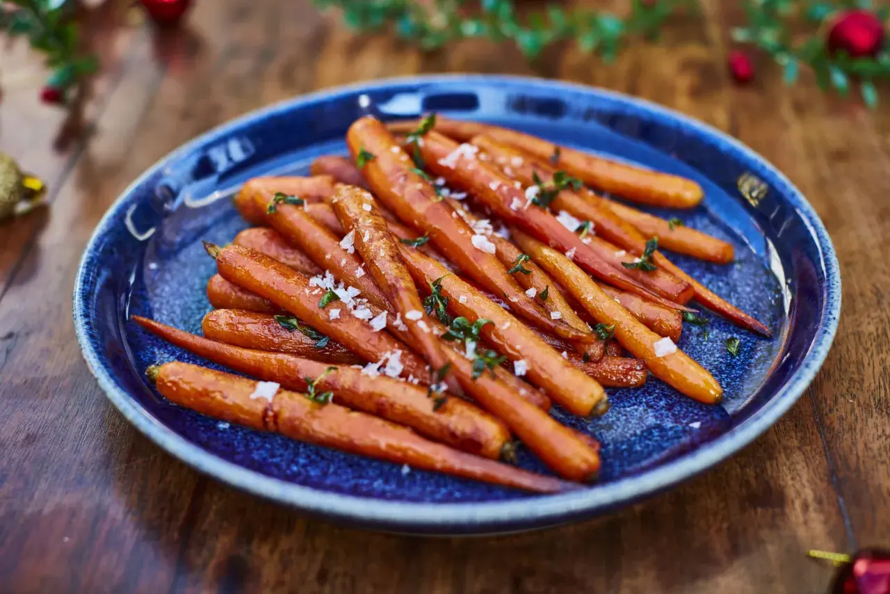 Zanahorias al horno, tiernas y doradas, espolvoreadas con sal marina y hierbas frescas, servidas en un plato azul sobre una mesa de madera.