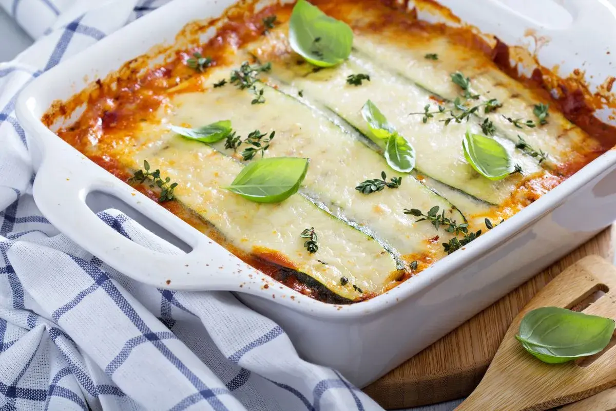 Pasticcio di zucchine appena sfornato, dorato e filante, guarnito con basilico fresco e timo.