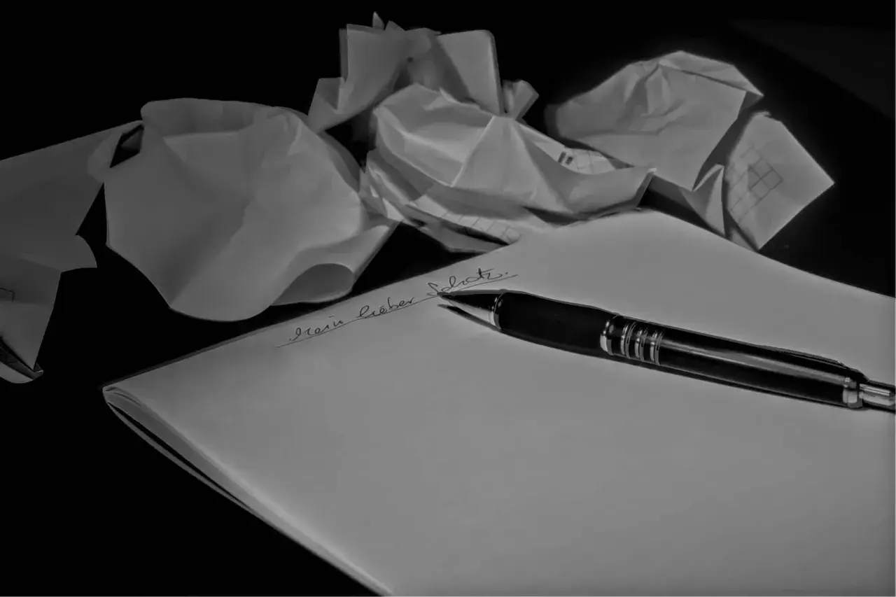 Carta accartocciata e penna su foglio bianco. La frase "Mein lieber Schatz" è scritta a mano.
