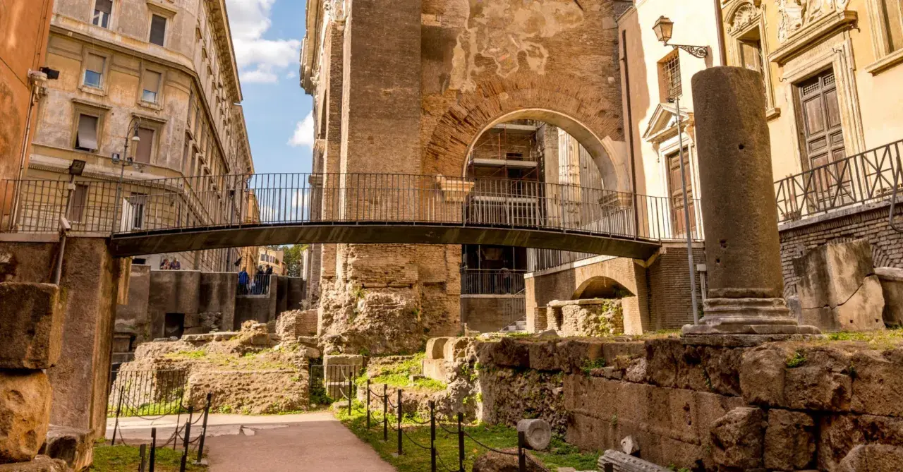 Antiche rovine nel ghetto ebraico di Roma, cosa vedere: un ponte moderno attraversa resti di colonne e mura di mattoni.