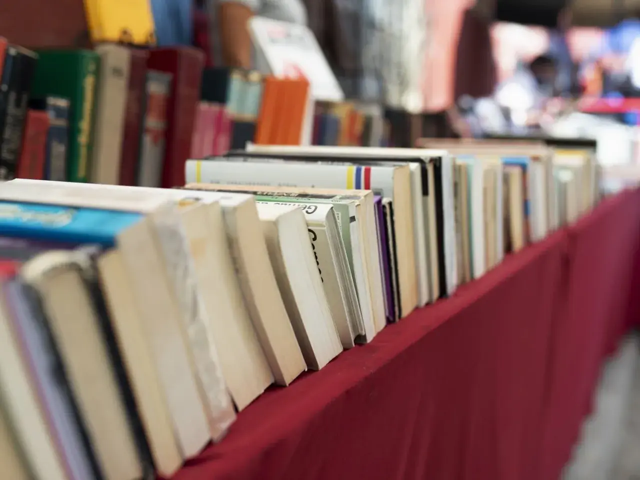 Rząd książek na czerwonym obrusie. Jak przygotować się do targów książki jako autor i czytelnik?