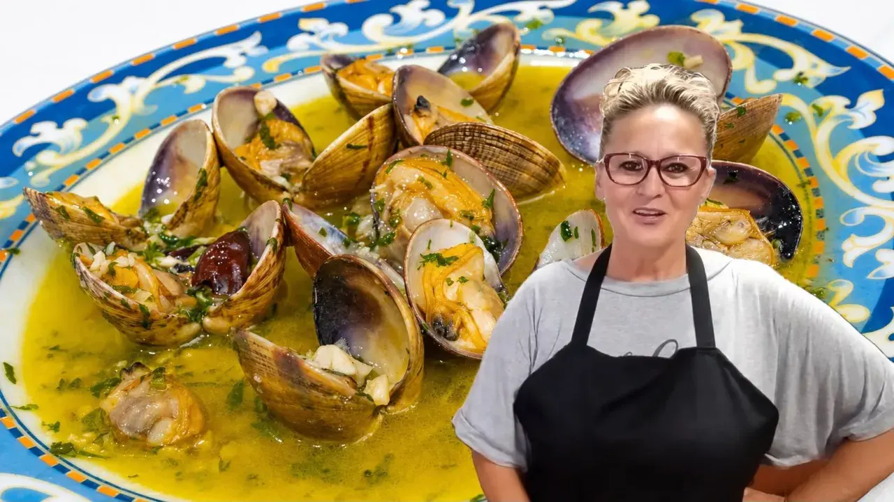 Una mujer sonriente presenta un plato de almejas al ajillo, conchas abiertas en una salsa dorada con perejil picado.