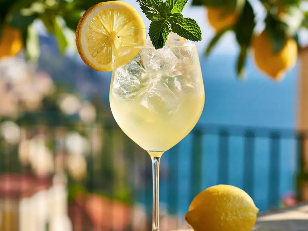 Erfrischender Limoncello Spritz mit Eis, Zitronenscheibe und Minze, garniert mit frischen Zitronen im Hintergrund.