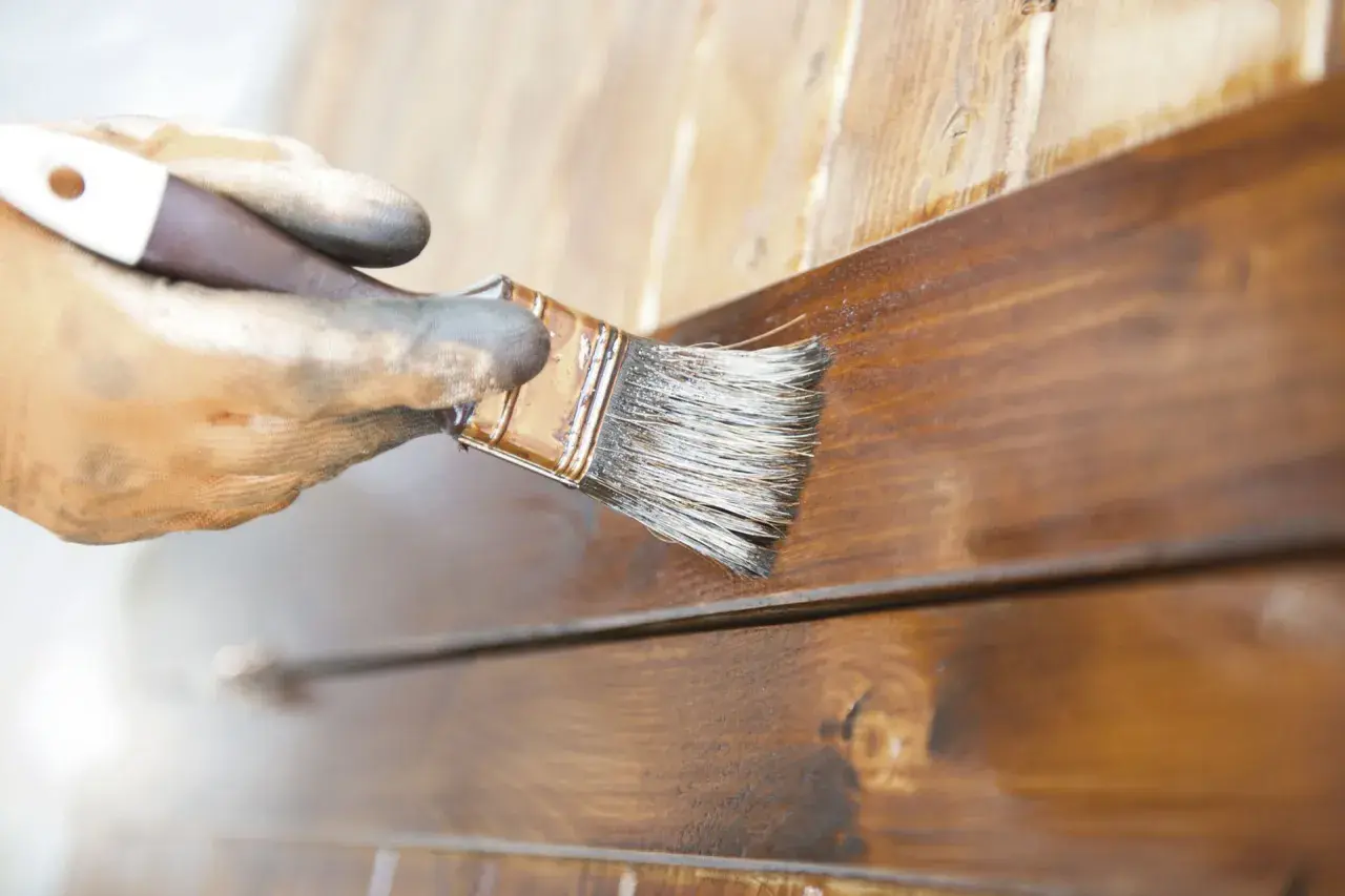 Mano enguantada aplica barniz a madera. El proceso de lijar entre capas de barniz asegura un acabado perfecto.