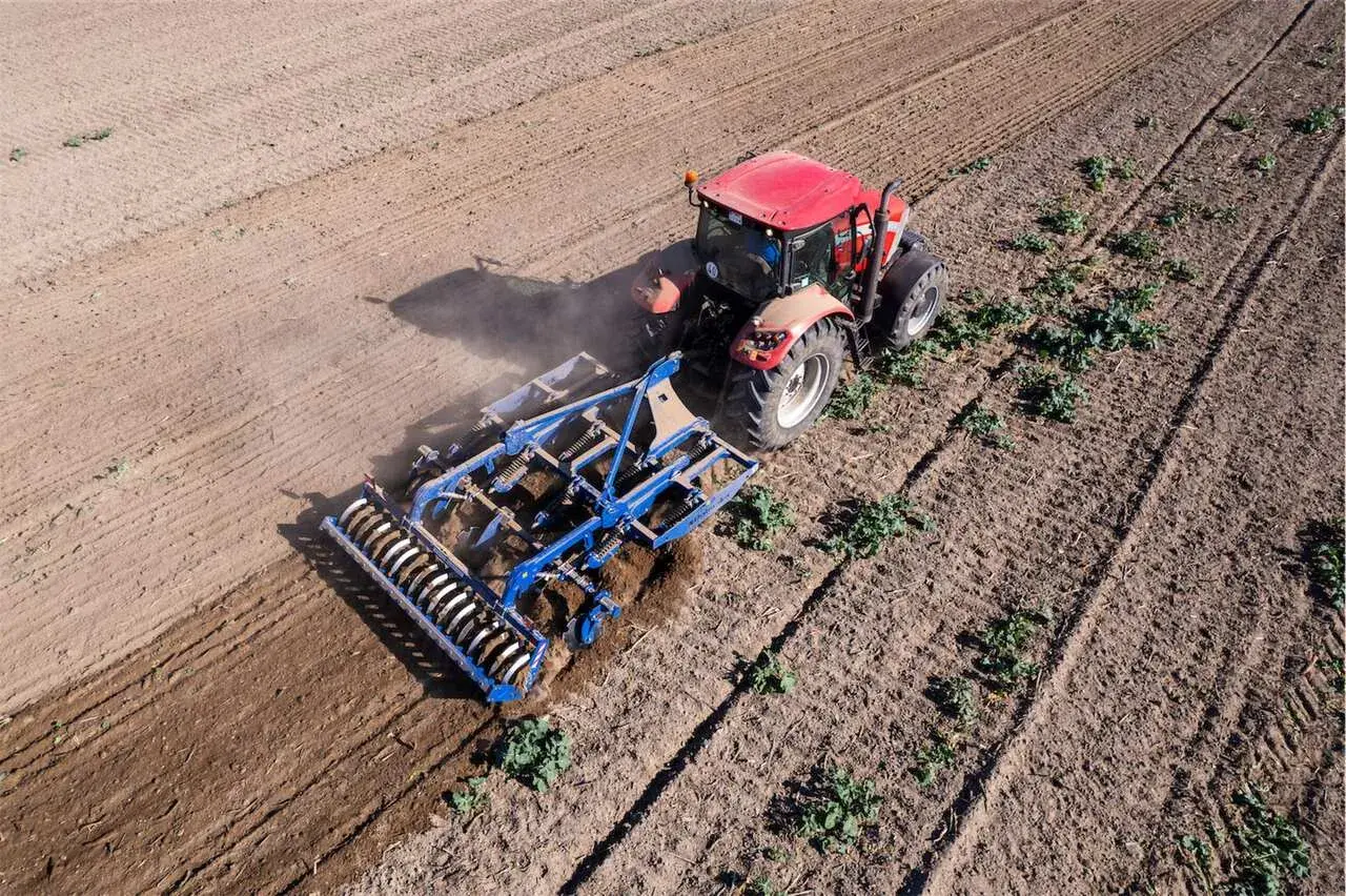 Un tracteur rouge travaille le sol avec un cultivateur, préparant le terrain pour la culture sans labour.