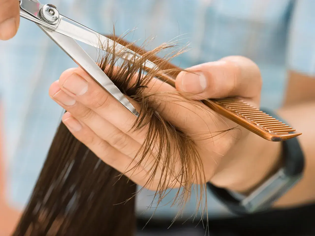 Manos cortando puntas abiertas con tijeras y peine. Pregúntate cada cuanto cortar el pelo para mantenerlo sano.