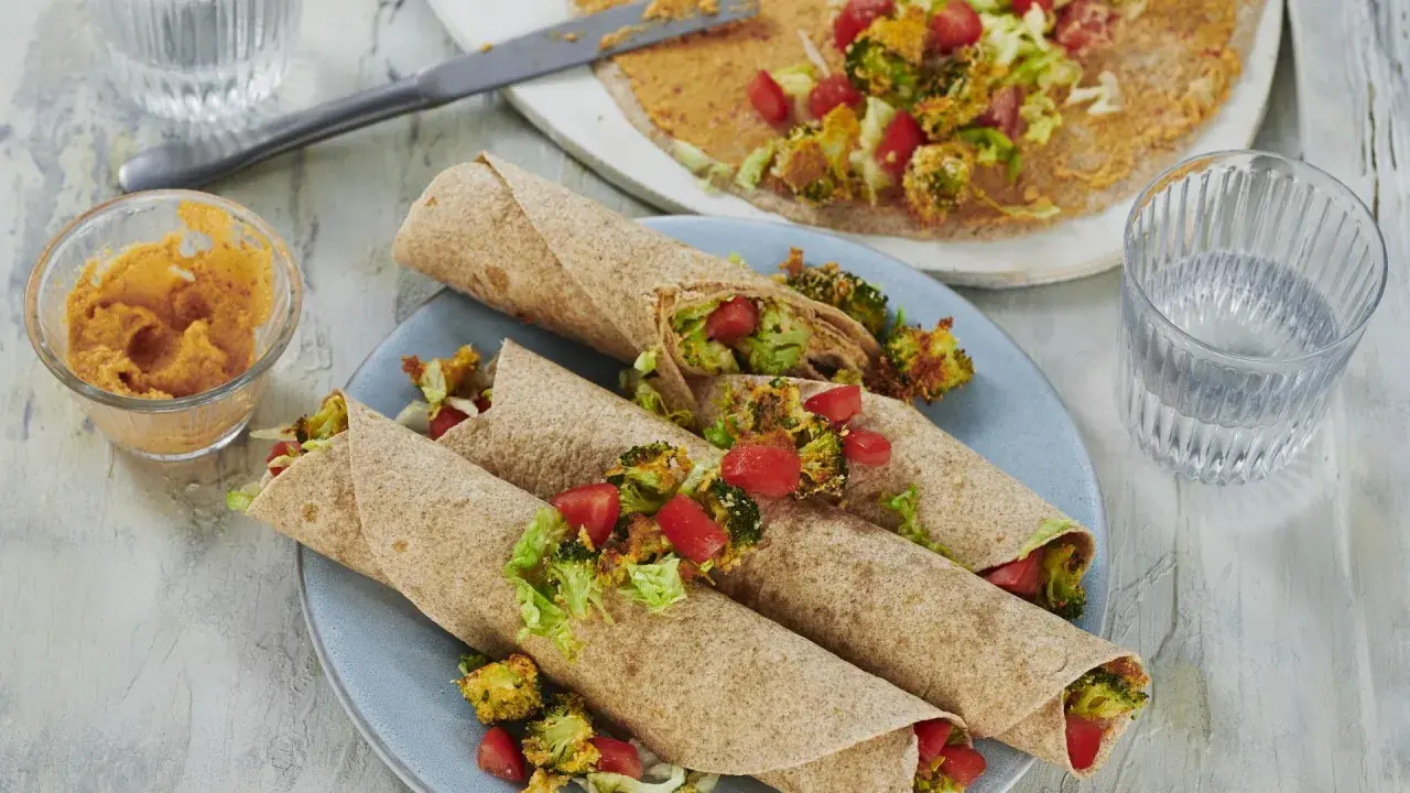 Leckere wraps vegetarisch gefüllt mit geröstetem Brokkoli, Tomaten und Salat. Dazu ein Dip und ein Glas Wasser.