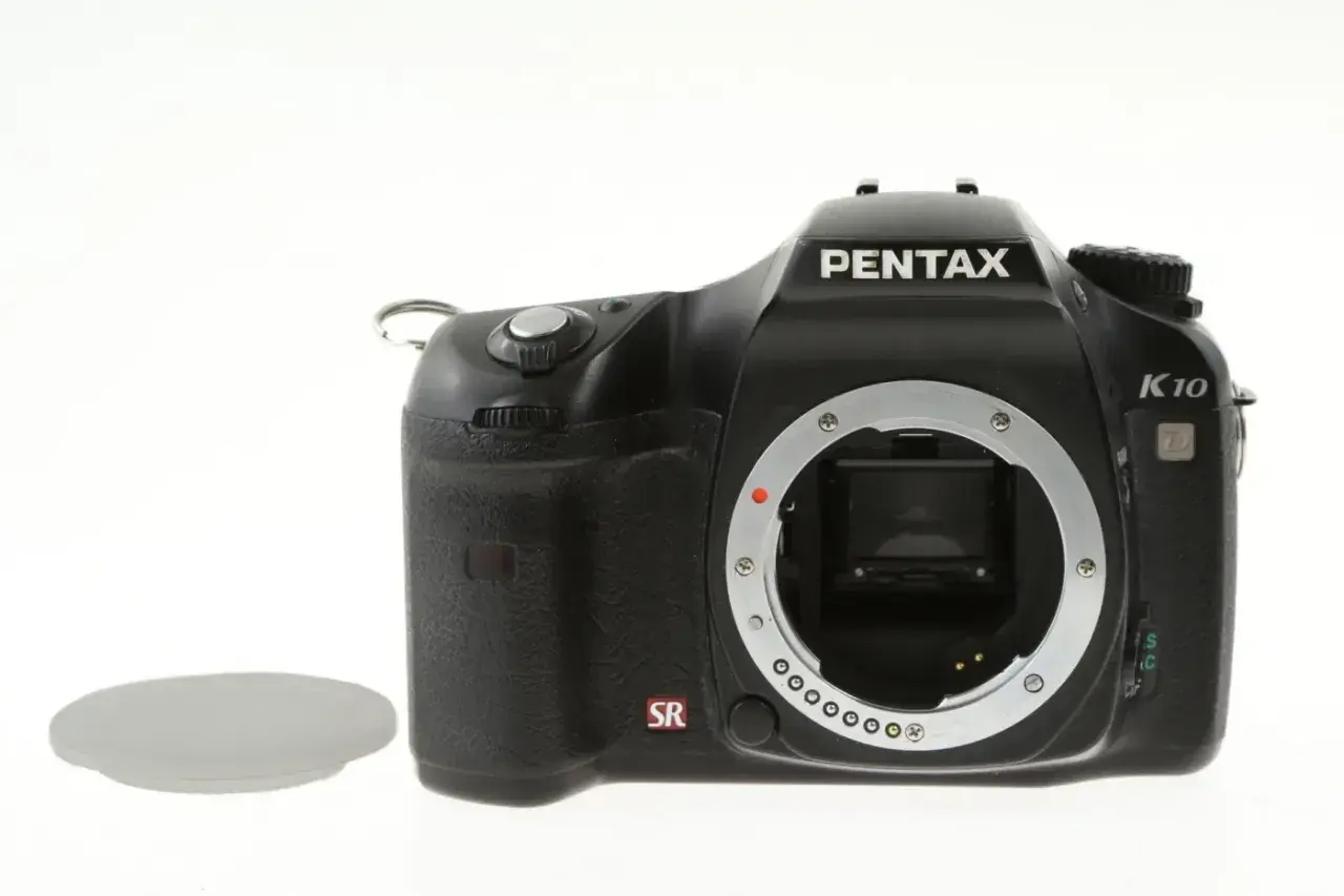 Czarny aparat Pentax K10 bez obiektywu, widoczna jego cmos matryca. Obok leży osłona.