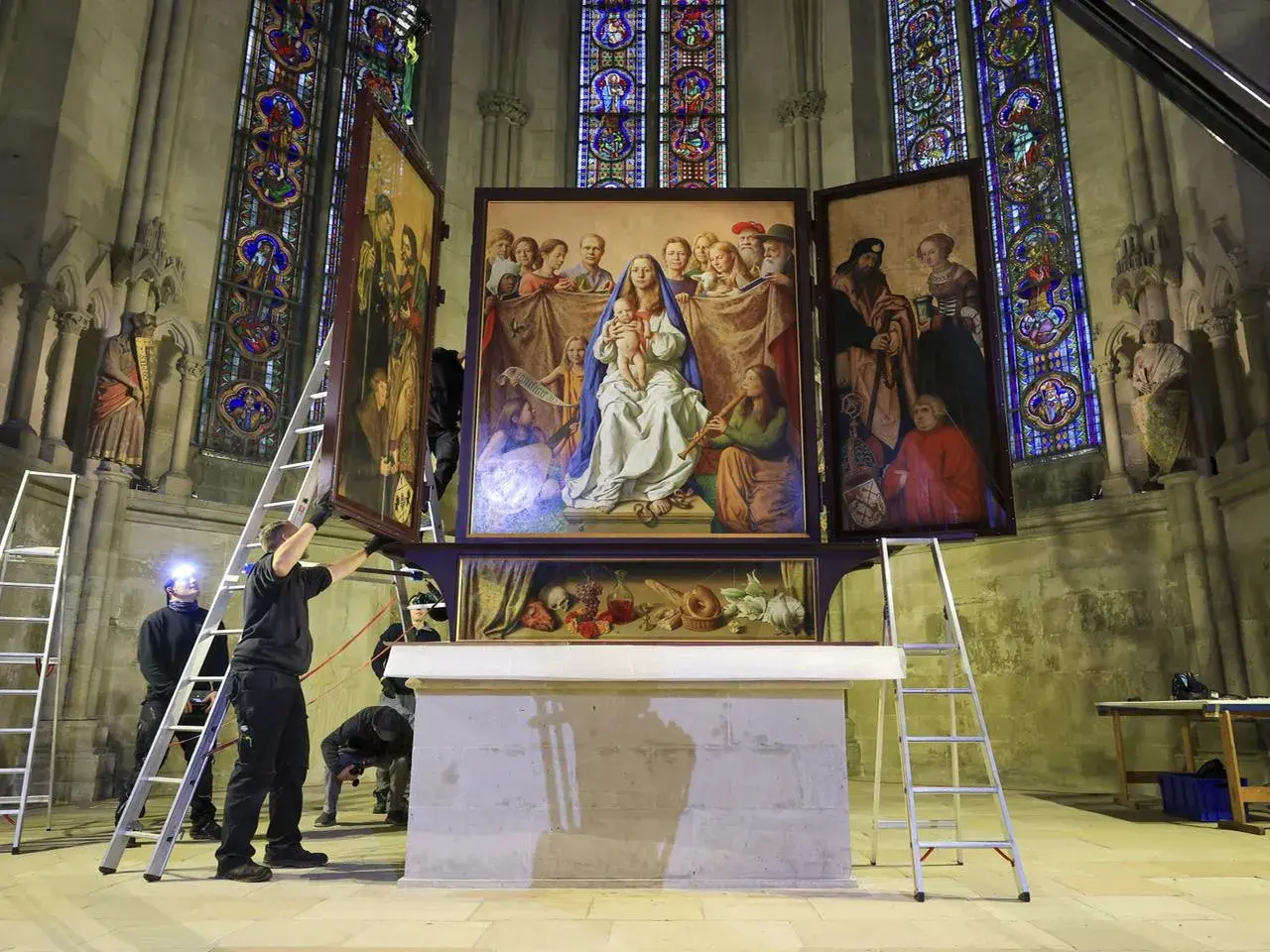Mitarbeiter montieren einen Flügel des Altars in der Kirche. Buntglasfenster und Skulpturen zieren die Kathedrale.