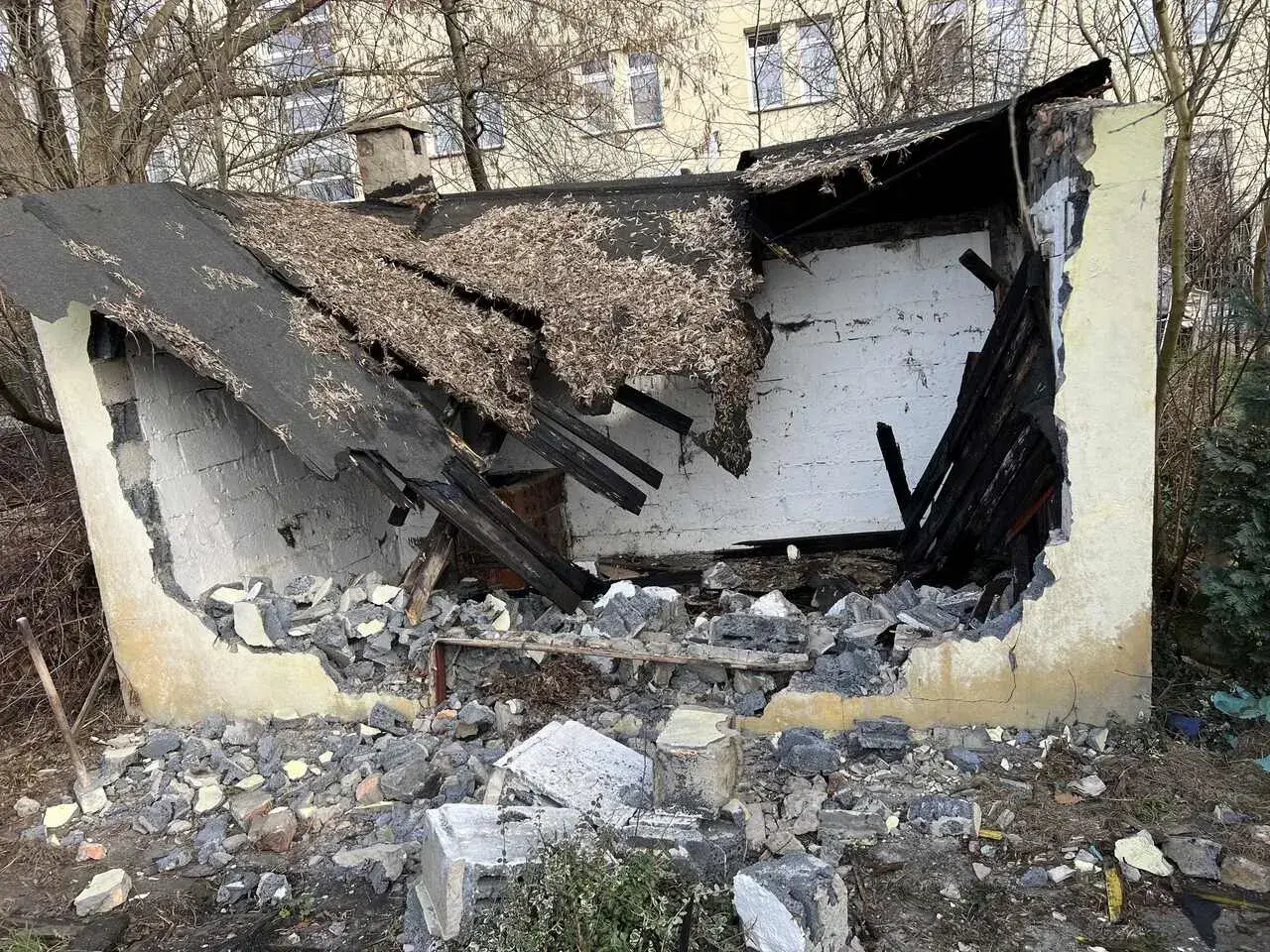 Zniszczony budynek po rozbiórce. Dach się zawalił, a ściany są wybite. Wokół leżą gruzy i drewniane belki.