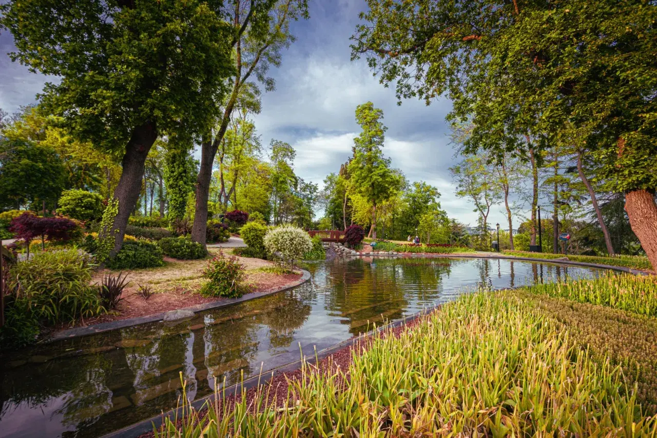 Malowniczy park z jeziorem, mostkiem i bujną zielenią.