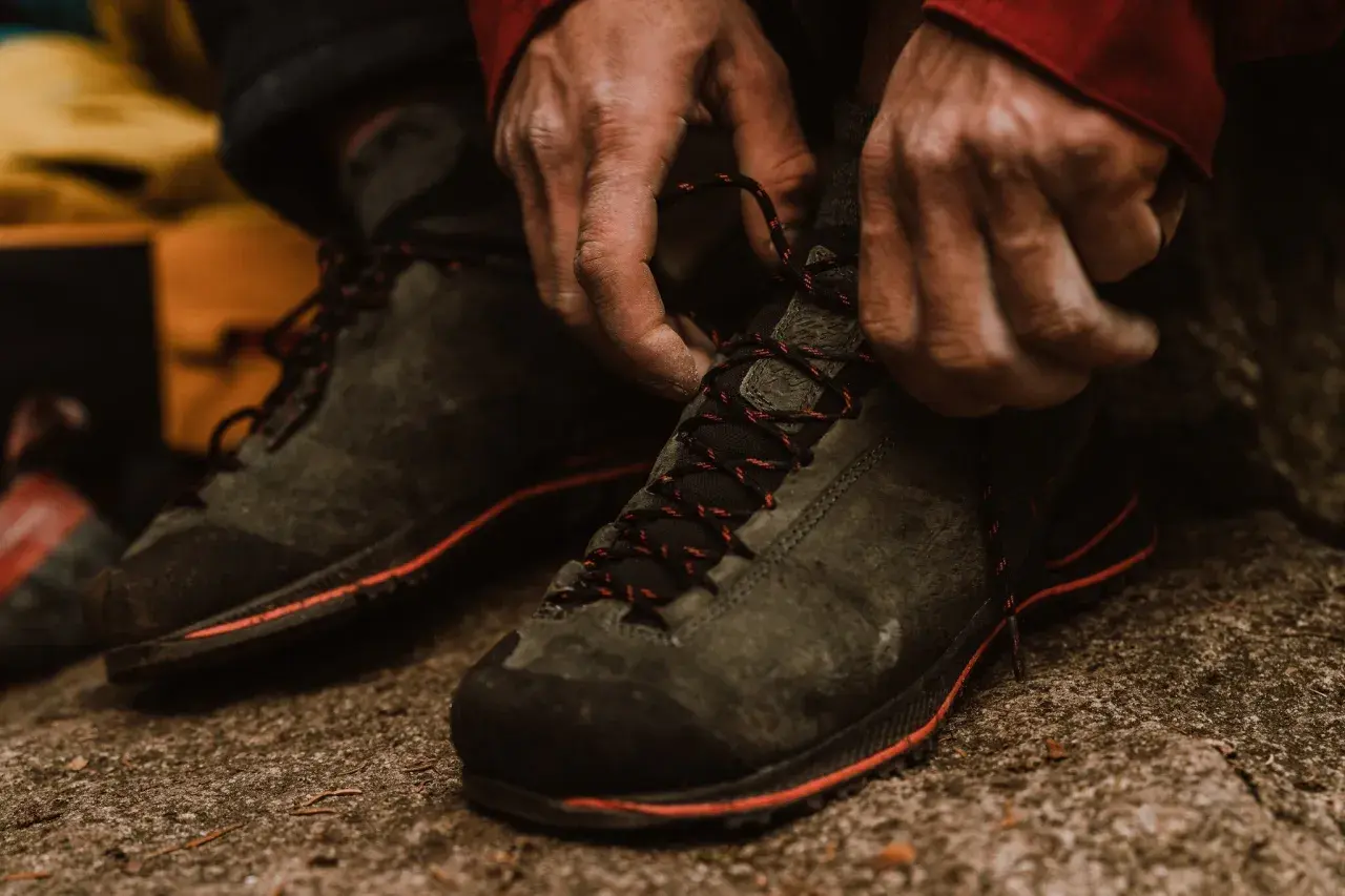 Hands tying red-laced hiking boots. Proper fit is crucial for comfort and performance on the trail.